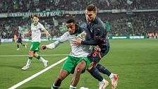Två fotbollsspelare kämpar om bollen nära sidlinjen på en upplyst arena.