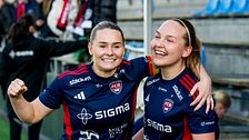 Två fotbollsspelare i blå matchställ firar tillsammans på en fotbollsarena.