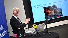 Man ger presentation med diagram på skärm, mikrofoner på bordet.