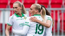 Fotbollsspelare i gröna shorts firar på planen. Röda stolar syns i bakgrunden.