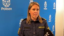 Polis i uniform intervjuas framför en blå bakgrund med polisens logotyp.