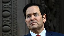 Marco Rubio i kostym framför utsmyckad mörk dörr.
