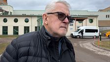 En person i en svart jacka står framför en byggnad med en vit minibuss i bakgrunden.
