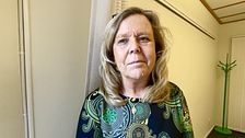 Kvinna i mönstrad klänning i kontorsmiljö, grön klädhängare i bakgrunden.