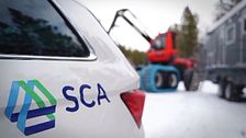 SCA-logotyp på bil med en skogsmaskin i bakgrunden på en snötäckt väg i skogarna kring Backe, i Strömsunds kommun.