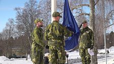 Tre militärer står vid en flaggstång där Natoflaggan håller på att hissas