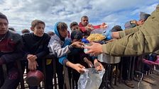 En grupp unga människor köar utomhus för att ta emot mat ur en stor gryta.