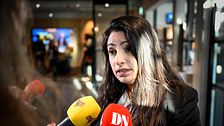 Person intervjuas av flera reportrar med mikrofoner från SVT och DN i en offentlig miljö.