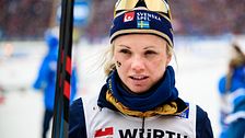 Skidåkare i tävlingsdräkt håller stav på snötäckt bana.