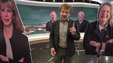 Person gestikulerar framför täckta ansikten på en tv-studio.