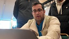 Tre personer observerar en datorskärm i ett inomhusmiljö.
