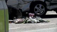 Blombuketter ligger på marken framför en bil