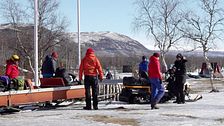 Flera personer är på väg att sätta sig i skoter och pulka för en av säsongens sista turer i Nikkaluokta.