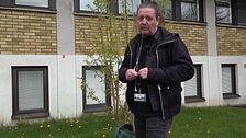 Person med ID-bricka står utomhus framför en byggnad med gula tegelväggar och fönster.