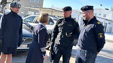 Uniformerad personal diskuterar utomhus framför byggnader. En bil syns i bakgrunden.