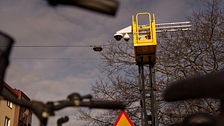 En gul kran med kamera är uppställt nära träd med cykelstyre synligt i förgrunden.