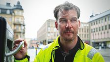 Person i gul jacka håller i ett sopkärl.