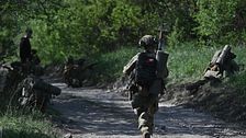 Soldater med utrustning rör sig längs en skogsväg under militäroperation.