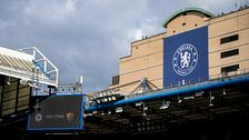 Chelsea FC:s klubbmärke syns på en byggnad vid Stamford Bridge under molnig himmel.