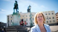 Kvinna i ljus kavaj på Göteborgs Gustav Adolfs torg med statyn i bakgrunden.