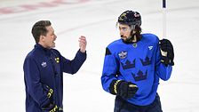 Hockeytränare ger instruktioner till spelare i Tre Kronor-tröja på isen.