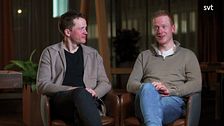 Två personer sitter i fåtöljer i en studio med dämpad belysning.