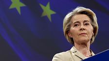 Kvinna vid talarstol framför EU-flagga med två synliga stjärnor i bakgrunden.