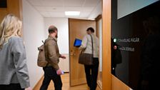 Tre personer går in i en rättssal med en digital skylt bredvid dörren.