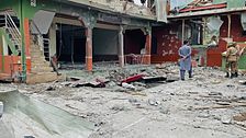 Två personer inspekterar raserade rester efter en explosion i ett kraftigt skadat hus.