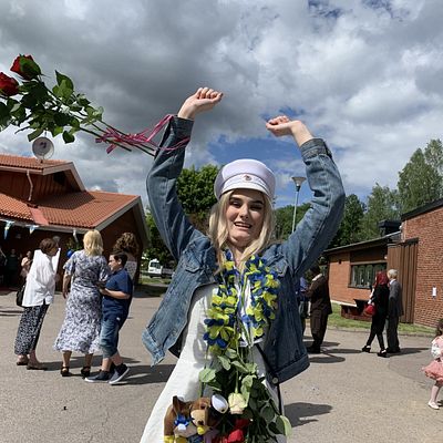 Marie Blomlie med vit studentmössa och ett fång rosor som flyger i luften.