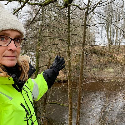 Karin Odén är geotekniker på SGI, Statens geotekniska institut står vid vattnet och visar hur lera rasat ner i Göta älv nära Lilla Edet.