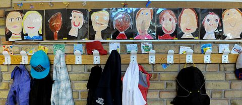 Skolkorridor utanför ett klassrum med kläder på klädhängare och tecknade porträtt av eleverna