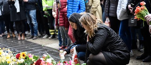 Två kvinnor står hukade framför ett blomsterhav för att hedra de som drabbades av terrorattacken på Drottninggatan i Stockholm 2017