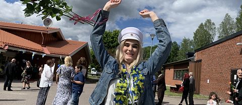 Marie Blomlie med vit studentmössa och ett fång rosor som flyger i luften.