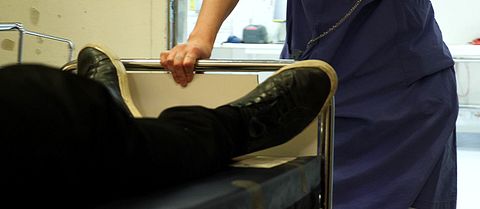 Närbild på ben på en patient som skjutsas i en sjukhussäng av personal i ett sjukhus.