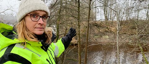 Karin Odén är geotekniker på SGI, Statens geotekniska institut står vid vattnet och visar hur lera rasat ner i Göta älv nära Lilla Edet.