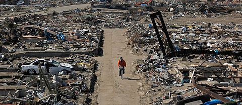 En överlevare cyklar genom ett område i Sendai som förstörts i tsunamin, den 1 april 2011.