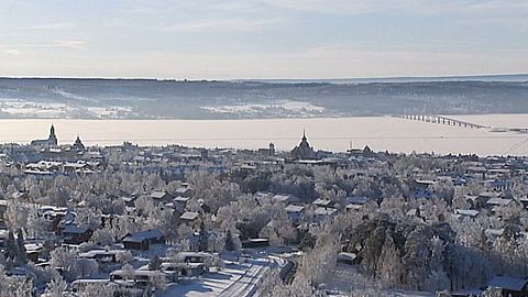 Vy över Östersund täckt av snö med dimma över sjö och Vallsundsbron i bakgrunden.
