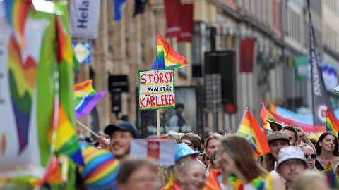 Pridetåg med regnbågsflaggor på en stadsgata. Skylt med texten ”Störst av allt är kärleken”