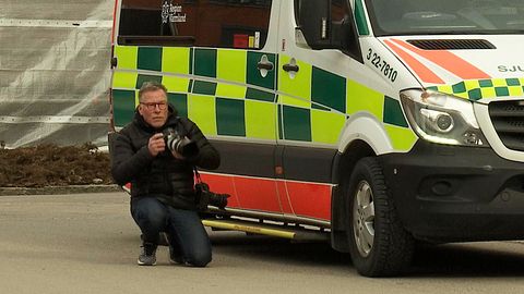 Fotografen Öyvind Lund står på knä bredvid en sjuktransportbil och fotograferar.