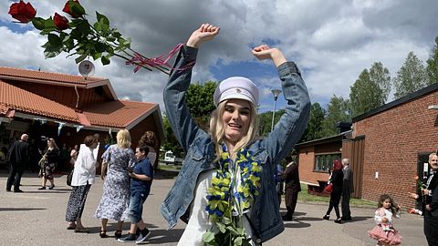 Marie Blomlie med vit studentmössa och ett fång rosor som flyger i luften.