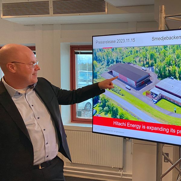 Vd:n för Hitachi Energy Sverige pekar på en bild av den nya fabriken på en tv-skärm.