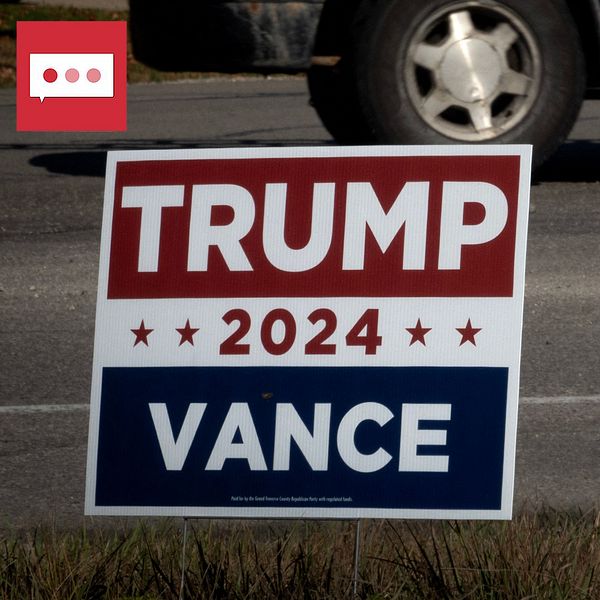Två kampanjskyltar i ett offentligt område. Till vänster en skylt med texten ”TRUMP 2024 VANCE” i rött, vitt och blått, och till höger en skylt med texten ”HARRIS for PRESIDENT WALZ” med en länk till kamalharris.com. Bakgrunden visar en väg med en del av en bil synlig.