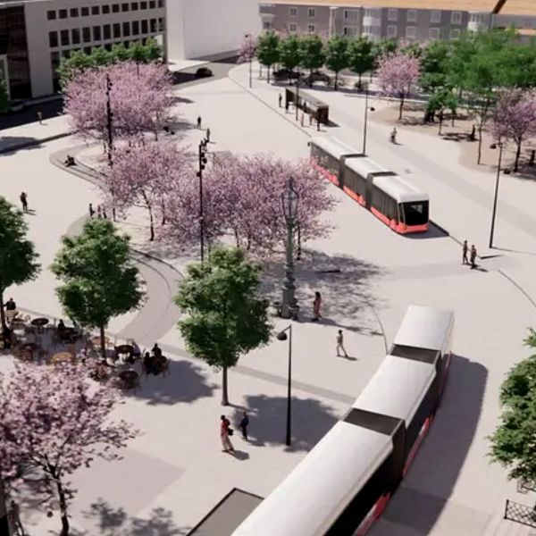 Skiss som visar planerna för kollektivtrafik på Östra torget i Jönköping. Blommande körsbärsträd och gröna träd. Det finns gående personer på trottoaren och en öppen plats, vilket visar en livlig stadsmiljö. Till höger Christin Stenberg, stadsbyggnadsdirektör Jönköping kommun, som står framför kameran, iförd en blå kappa och en sjal.