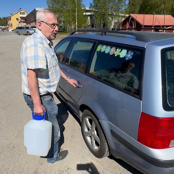 En man håller i en vattentank utanför en bil