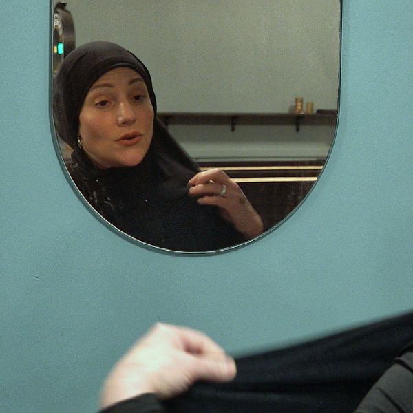 En kvinna sätter på sig en svart bomullsslöja och tittar sig i spegeln.