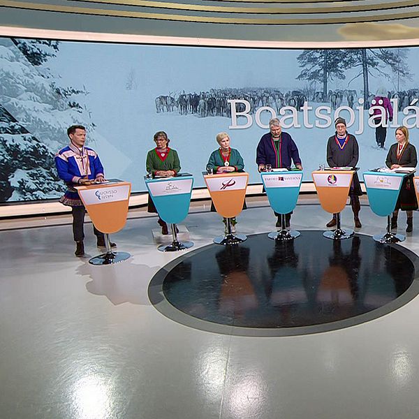 Åtta deltagare i samiska kläder i en tv-studio med vinterlandskap i bakgrunden. Bild från SVT:s partiledardebatt inför val till Sametinget 18 maj.