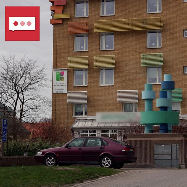 En byggnad med färgglada fönsterluckor och en modern entré. Framför entrén står en skulptur bestående av geometriska former i olika färger. Två personer går in i byggnaden medan en bil är parkerad i närheten. Träd och grönska syns i omgivningen.