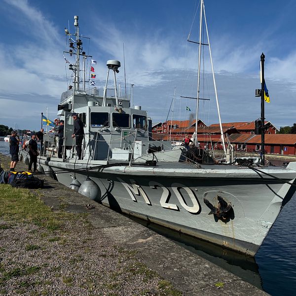 Fartyg står töjt längst en kanal. På fartygets sida står det ”M 20”.