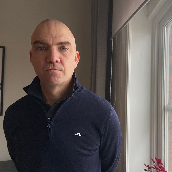 Stefan Dalteg står vid ett fönster med utsikt över stadsmiljö. Han tittar allvarligt in i kameran.